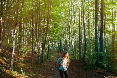 Genç kadın sonbaharda gün batımı ışığında ormanda bir sırt çantası taşıyan, ormanda bir yürüyüş.
