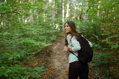 Genç kadın sonbaharda gün batımı ışığında ormanda bir sırt çantası taşıyan, ormanda bir yürüyüş.
