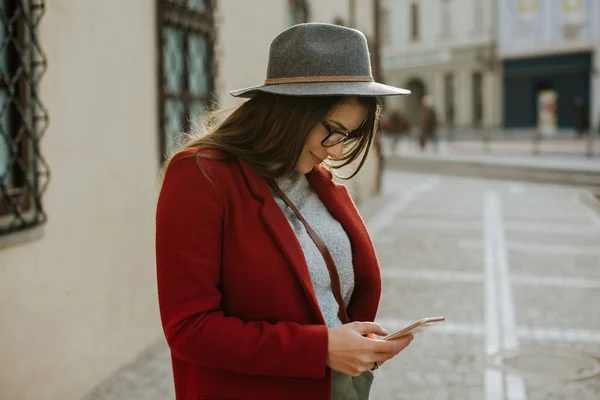 年轻的时尚妇女戴着眼镜拿着智能手机 戴着帽子 在老城区 — 图库照片
