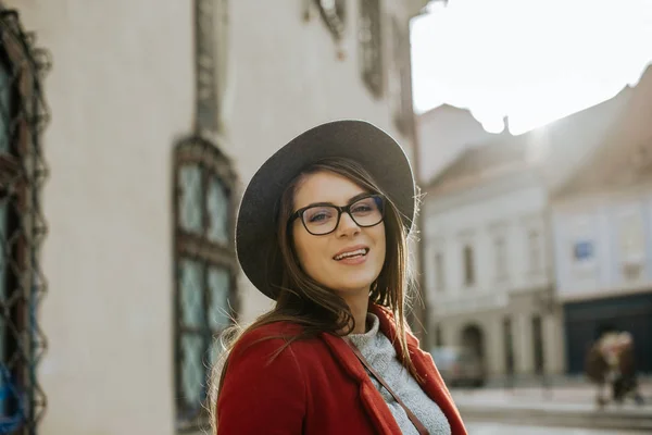 Young hipster woman with eyeglasses wearing a hat, looking at camera in the city old town, Europe