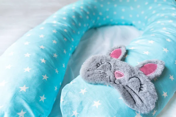 Light blue supporting pillow with stars on white sheet in bed for comfortable sleep of pregnant woman. Funny sleeping mask in form of bunny,cat with eyes,ears,mouth. Accessories for expectant mothers.