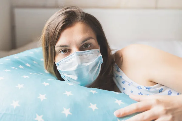 Pregnant woman sleeps in nightgown, medical face mask in bed on blue comfortable supporting pillow with stars. Accessories for expectant mothers.Afraid of coronavirus, covid -19 in hospital.Self care.