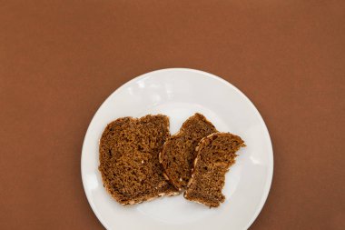 Dilimlenmiş çavdar ekmeği beyaz plare ve kahverengi zemin üzerinde. Bütün tahıl çavdar ekmeği tohumları ile