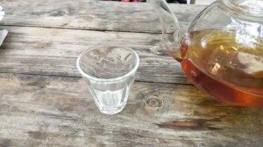 Ahşap masa bardakta çay dökülen çaydanlık.