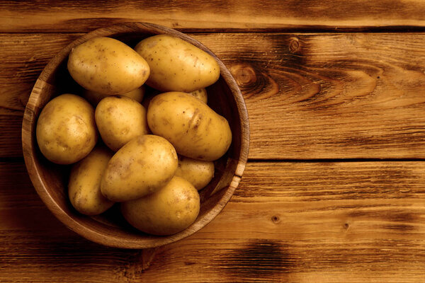 Raw new potatoes in a wooden dish on wooden background
