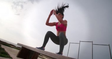 Genç kaslı kadın bankta zıplıyor ve çömeliyor.