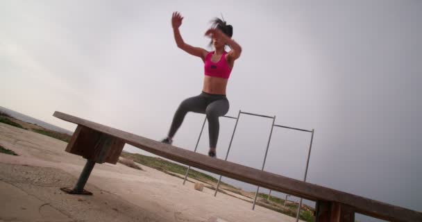 Junge Sportlerin springt auf Bank und macht Kniebeugen im Freien — Stockvideo