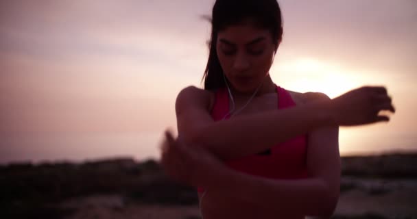 Mujer joven en forma con auriculares que estiran sus brazos al aire libre — Vídeos de Stock