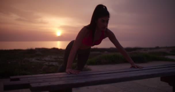 Tânăra femeie atletică face împingeri împotriva băncii la apusul soarelui — Videoclip de stoc