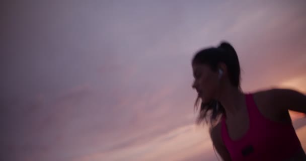 Молода брюнетка бігунка слухає музику на заході сонця — стокове відео