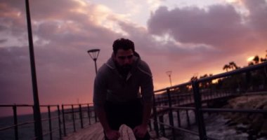Gün batımında deniz kenarında koşan yorgun genç bir erkek sporcu.