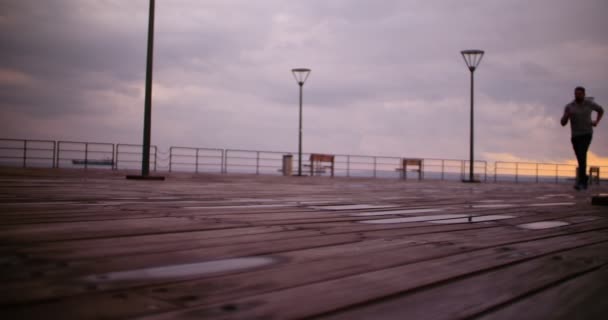 Junger fitter Mann joggt im Morgengrauen am Meer — Stockvideo