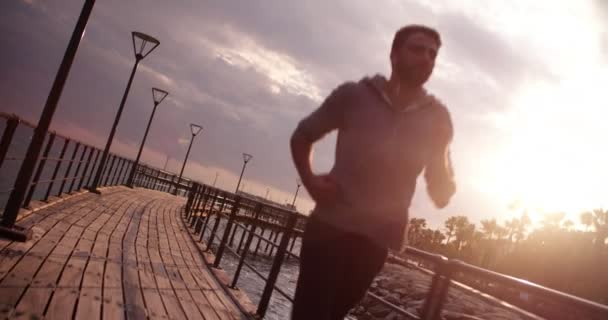 Joven hombre en forma corriendo y escuchando música al atardecer — Vídeos de Stock