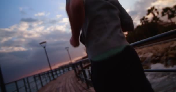 Młody sprawny mężczyzna biegający na pomoście o zachodzie słońca — Wideo stockowe