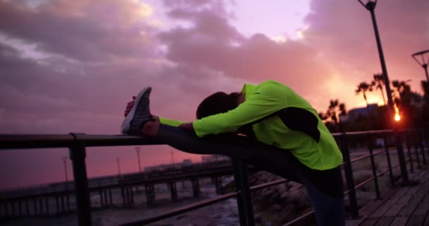 Μια γυμνασμένη νεαρή γυναίκα ζεσταίνει τα πόδια της το ηλιοβασίλεμα. — Αρχείο Βίντεο