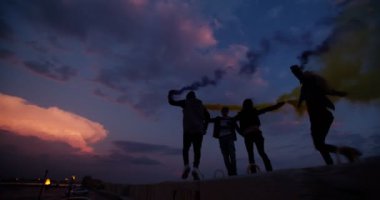 Bir grup genç arkadaş gün batımından sonra sis bombalarıyla kutlama yapıyorlar.