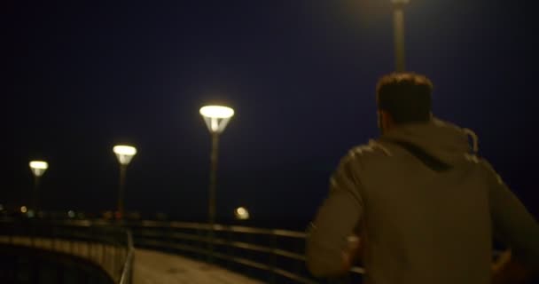 Musuclar young man running on a pier at night — Stock Video