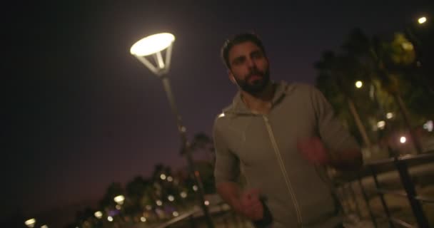 Mladý atletický muž běží v noci a poslouchá hudbu — Stock video