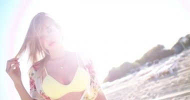 Bikinili sarışın bir kadın ve sahilde yürüyen bir örtü.