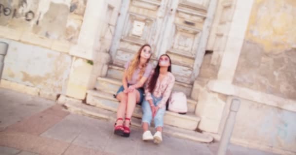 Hipster γυναίκες φυσάει ροζ τσιχλόφουσκες σε παλιούς δρόμους της ευρωπαϊκής πόλης — Αρχείο Βίντεο