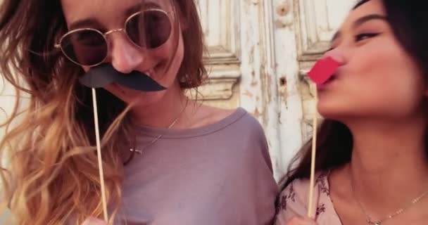 Young women holding mustaches and lips on sticks having fun — Stock Video