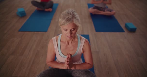 Старша жінка розслабляється під час зосереджених вправ з дихання в класі йоги — стокове відео