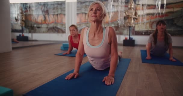 Όμορφη ηλικιωμένη γυναίκα που τεντώνεται σε στρώμα γυμναστικής στην τάξη γιόγκα — Αρχείο Βίντεο