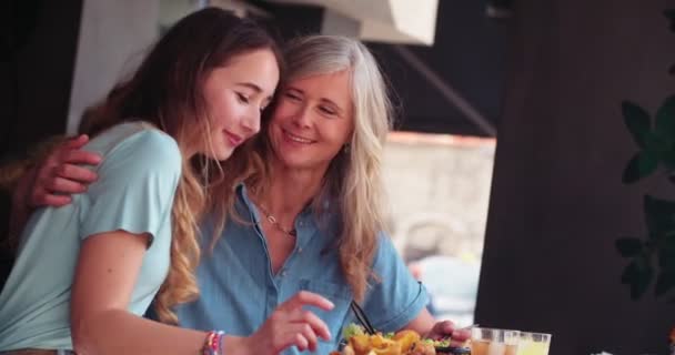 Liefdevolle volwassen moeder en dochter delen van een maaltijd en knuffelen — Stockvideo