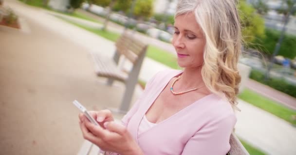Mulher sênior bonita no parque mensagens de texto em seu smartphone — Vídeo de Stock