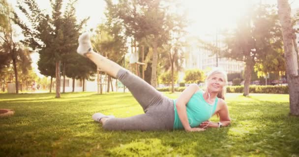 Ajuste a mulher sênior ouvir música e exercício na grama — Vídeo de Stock