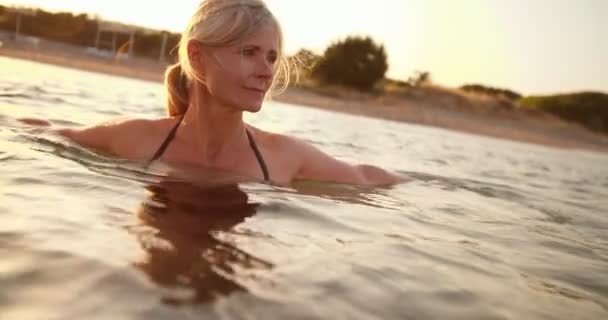 Hermosa mujer mayor nadando en el mar al atardecer — Vídeos de Stock