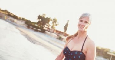 Mayolu yaşlı kadın gün batımında sahilde yürüyor.