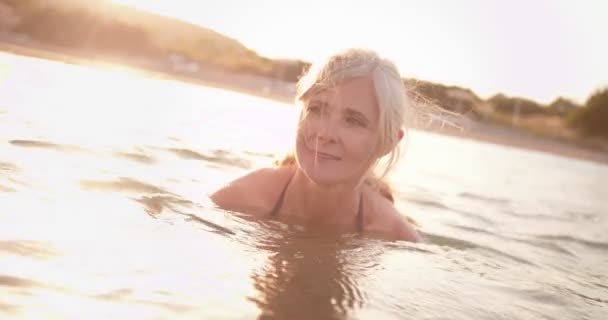 Mulher idosa ativa nadando no mar ao pôr do sol — Vídeo de Stock