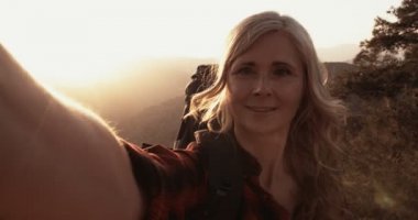 Yaşlı kadın yürüyüşçü dağ yamacında selfie çekiyor.