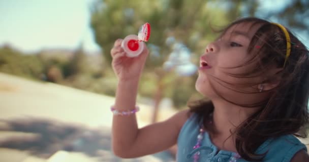 Feliz niña soplando burbujas en el patio de recreo en verano — Vídeos de Stock