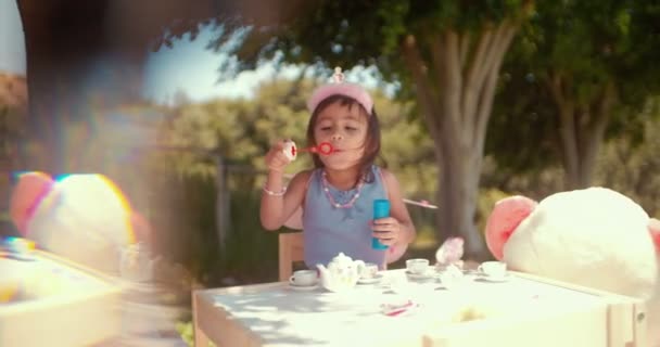 Маленькая азиатка пускает пузыри на чаепитии в саду — стоковое видео