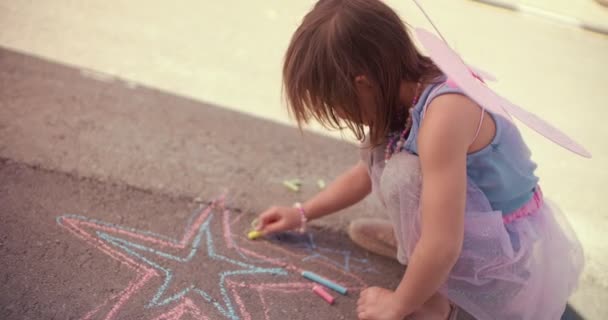 Ενθουσιασμένο κοριτσάκι που παίζει και ζωγραφίζει με κιμωλία στην άσφαλτο — Αρχείο Βίντεο