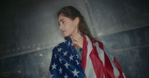 Mujer joven de pie con bandera americana envuelta alrededor de sus hombros — Vídeos de Stock