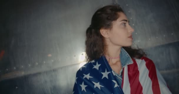 Ελκυστική νεαρή κοπέλα με αμερικανική σημαία στέκεται ενάντια στον αστικό τοίχο — Αρχείο Βίντεο
