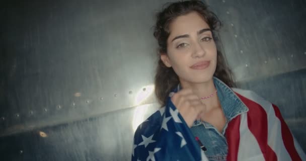 Linda morena sorridente de pé com bandeira americana enrolado em torno dela — Vídeo de Stock