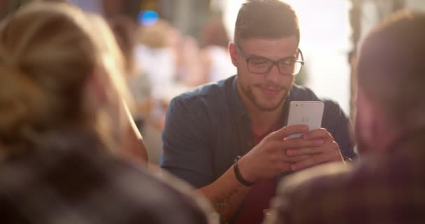 Jonge hipster man met behulp van mobiele telefoon in cafe met vrienden — Stockvideo
