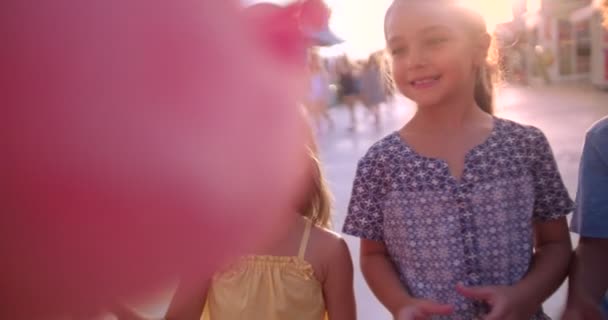Багатоетнічні діти їдять бавовняні цукерки в парку розваг — стокове відео