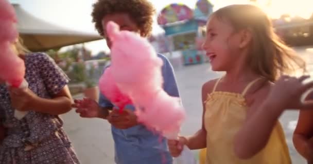 Többnemzetiségű gyerekek vattacukrot és popcornt esznek a vidámparkban — Stock videók