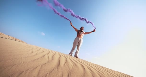 Junger Mann steht mit Rauchbomben in Wüste — Stockvideo
