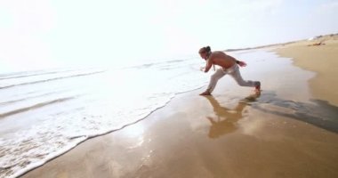 Genç atletik adam deniz kenarında ters takla atıyor.