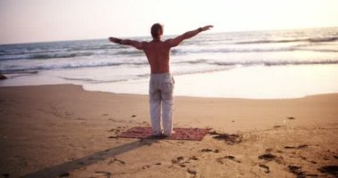 Yoga yapan bir adam gün batımında okyanusta poz verir.