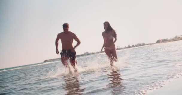 Fiatal hipszter pár a nyári szünetben fut a tengerben — Stock videók
