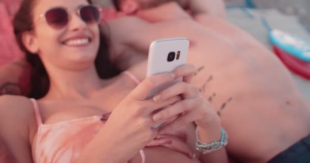 Пара хипстеров загорает на пляже и пишет смс на мобильный телефон — стоковое видео