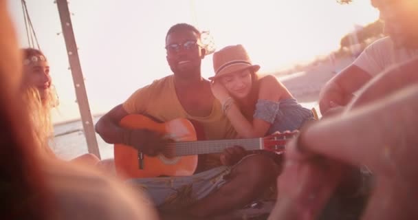 Plaj partisinde akustik gitar dinleyen çok ırklı genç hipsterler. — Stok video