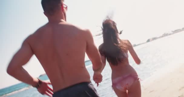 Genç romantik çift el ele tutuşup denize koşuyor. — Stok video